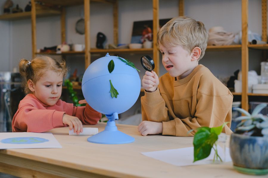 Dos niños observando un globo terráqueo con una lupa